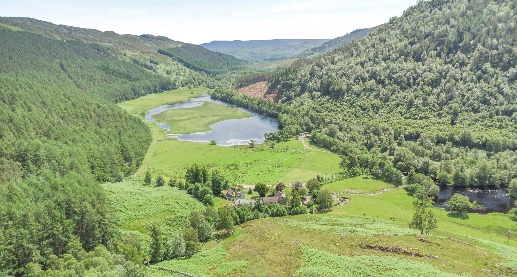 Aerial view over forested hills, the loch and the river winding through the glen