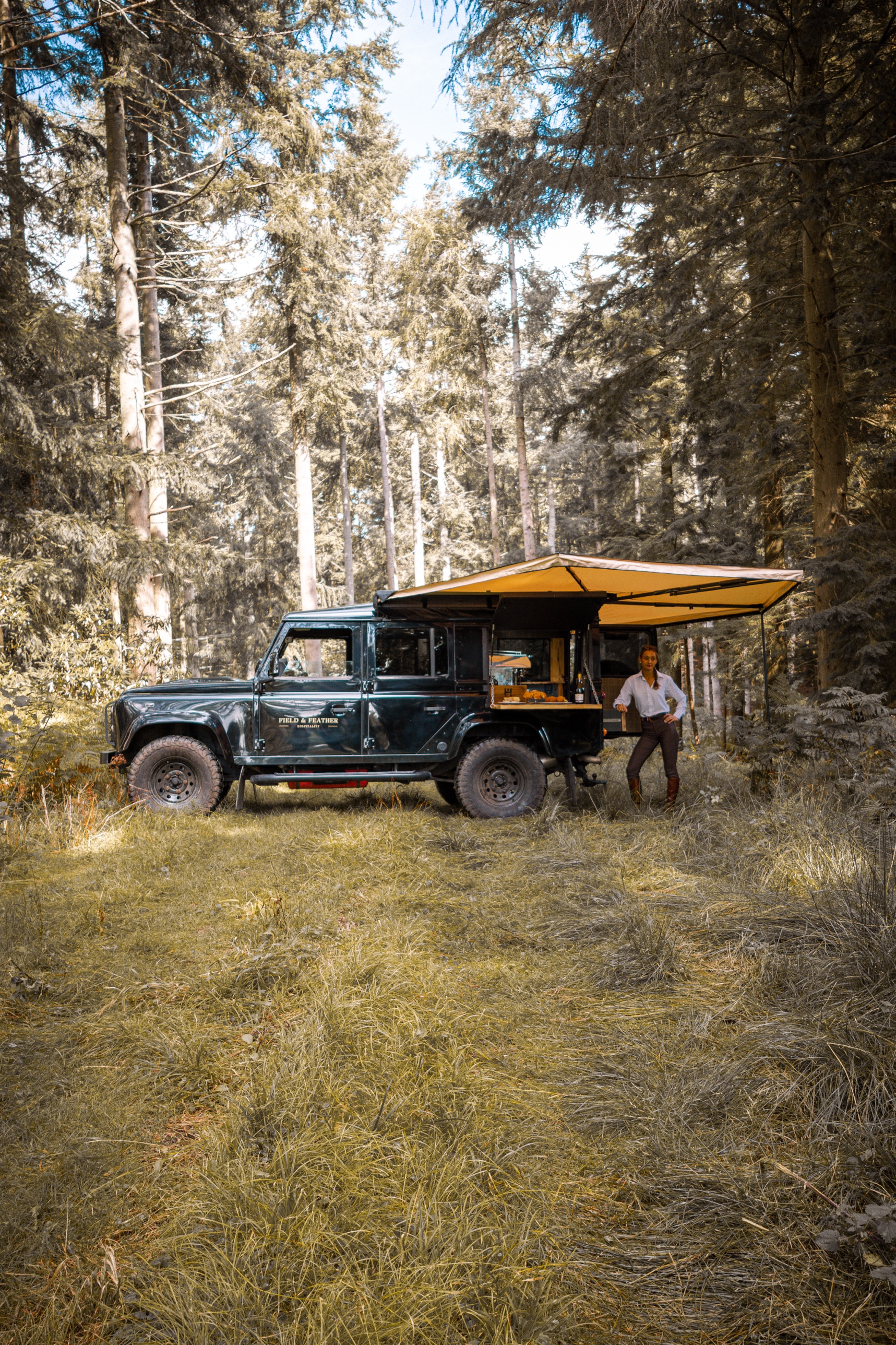 The Defender 110 hospitality vehicle with its awning extended in woodland